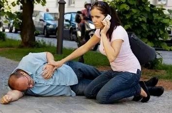 A bystander calling 911 on a mobile phone while kneeling beside an unresponsive person.