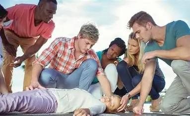 Bystanders performing chest compressions on an unresponsive person while others assist.