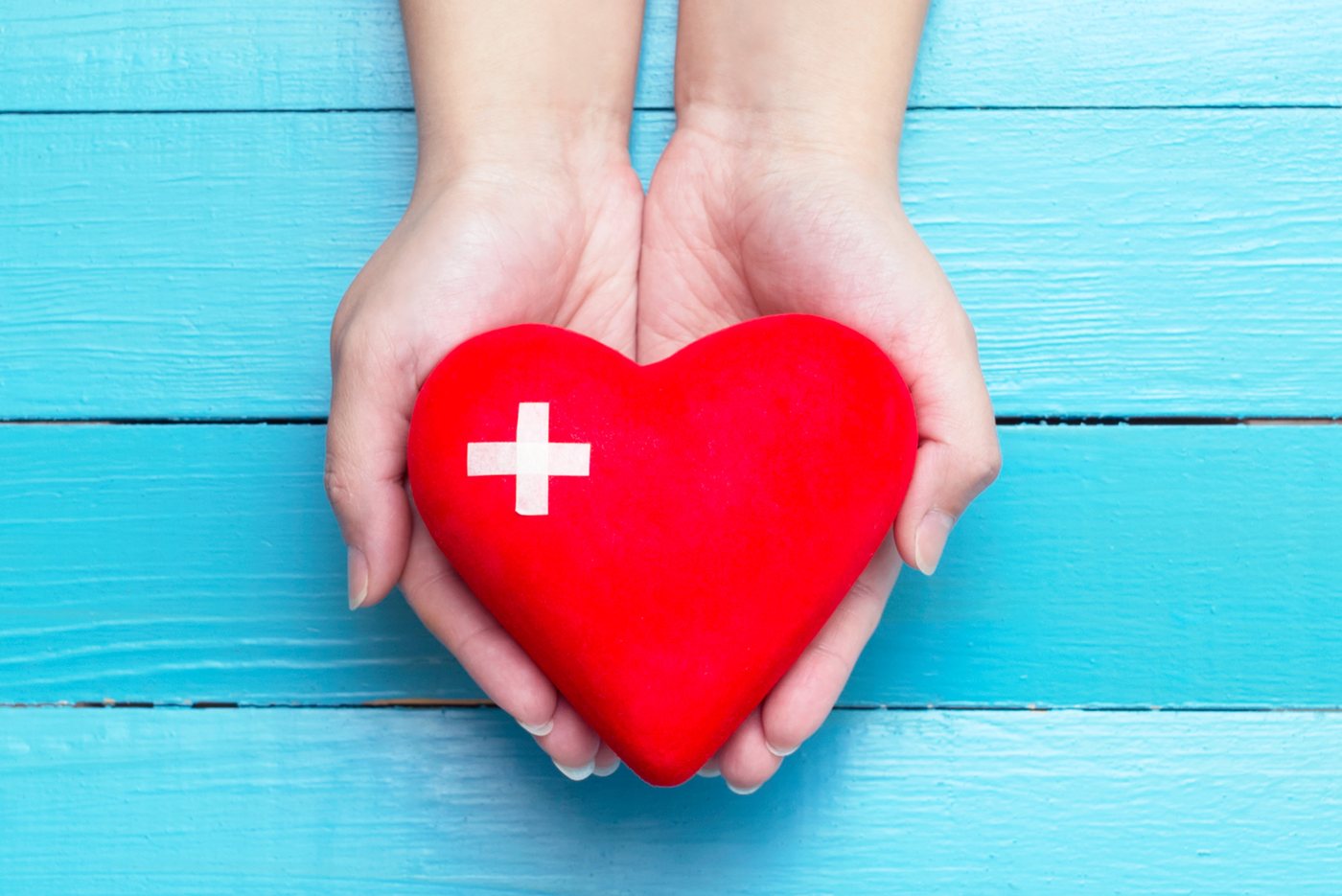 Two hands holding a red heart marked with a white first-aid cross.
